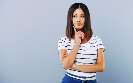 Not sure Give it some extra thought. Studio shot of an attractive young woman looking thoughtful against a grey background.の写真素材