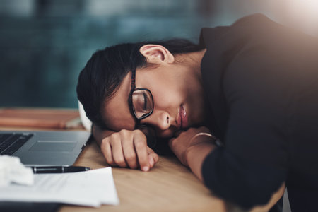 I just need to rest my eyes for a few minutes. a young businesswoman sleeping at her desk while working in an office.の写真素材