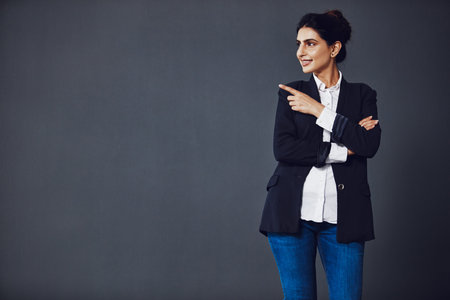 For your information. Studio shot of an attractive young businesswoman pointing at copy space against a dark background.の写真素材