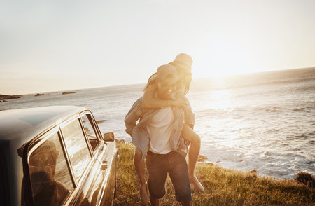 Roadtrippers in their element. a happy young couple enjoying a piggyback ride on a road trip.の写真素材