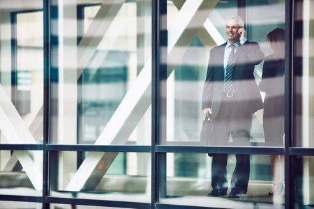 Its all about who you know. a mature businessman using a mobile phone in a modern glass office.の写真素材