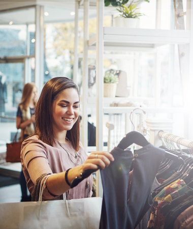 This is the last one so its now or never. a young woman holding up an item that she picked out in a clothing store.の写真素材