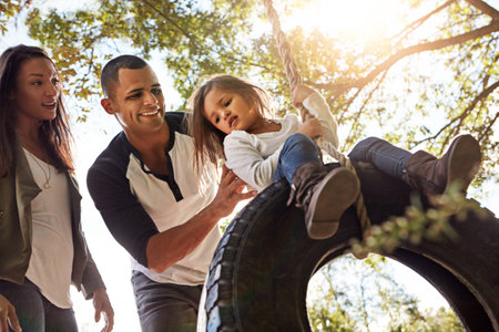 The bond of a family is priceless. a happy mother and father pushing their daughter on a tyre swing.の写真素材