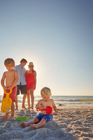 They never get bored on the beach. two little boys playing on the beach with their parents in the background.の写真素材