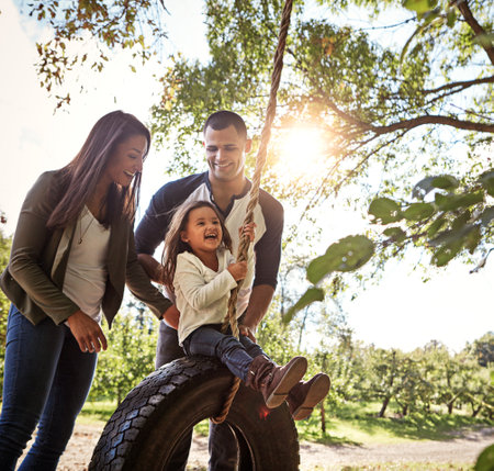 Connecting as a family. a happy mother and father pushing their daughters on a tyre swing.の写真素材