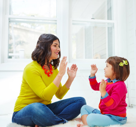 Pat a cake, pat a cake. an adorable little girl playing a clapping game with her mother at home.の写真素材