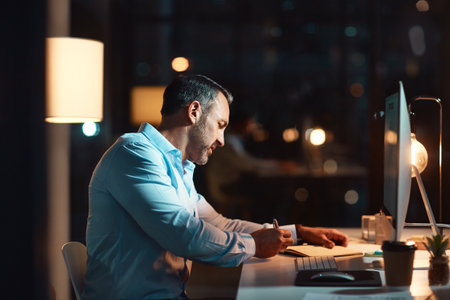 Completely committed to the deadline. a mature businessman using a computer during a late night at work.の写真素材