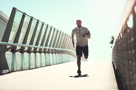 Be determined to get fit and make it happen. a handsome young man running on a bridge in the city.の写真素材