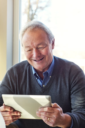 Having appsolute fun. a senior man using a tablet at home.の写真素材