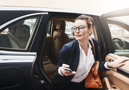 I have to hurry or Ill be late. a confident young businesswoman getting out of a car while holding a cellphone outside during the day.の写真素材