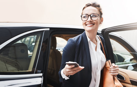 Finally at work. a cheerful young businesswoman getting out of a car while holding a cellphone outside during the day.の写真素材