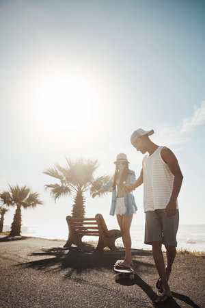 Becoming the new skater girl in town. a young man teaching his girlfriend how to skateboard on the promenade.の写真素材