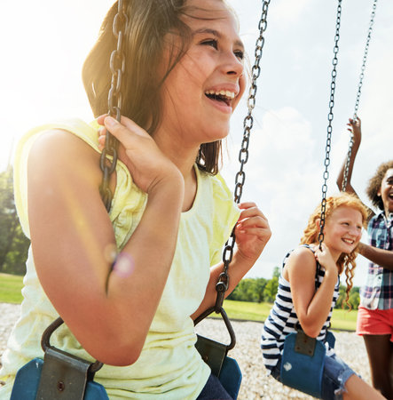 Fun times are in full swing. young girls playing on the swings at the park.の写真素材