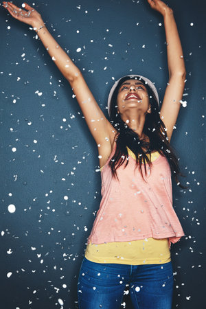 Lifes too short not to celebrate it. Studio shot of an attractive young woman having fun with confetti against a dark background.の写真素材