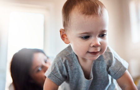 Ready or not, here I come. an adorable baby girl crawling on a bed with her mother in the background.の写真素材