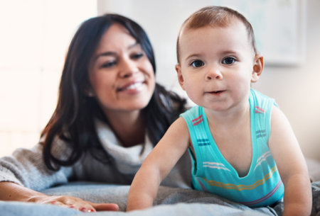 Watch out world, here I come. an adorable baby girl crawling on a bed with her mother in the...