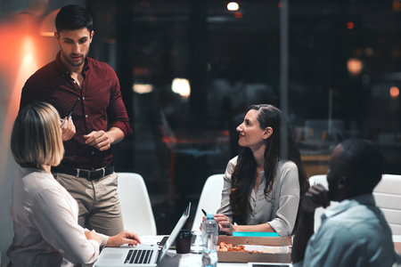 The whole team is on board for the night shift. colleagues having a meeting during a late night in a modern office.の写真素材