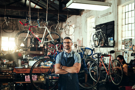 Striving to provide superior bicycle repair service. Portrait of a mature man working in a bicycle repair shop with his coworker in the background.の写真素材