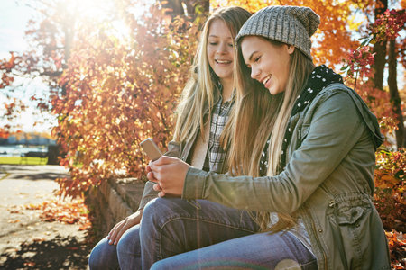 Modern age connections. two young friends using a mobile phone together while out in the park.の写真素材
