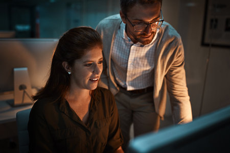 Theyve never missed a single deadline. two businesspeople working late on a computer in an office.の写真素材