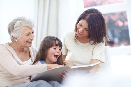 And they lived happily ever after...a little girl sitting with her mother and grandmother and reading a book.の写真素材