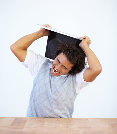 Angry, laptop and frustrated businessman smash his computer due to stress isolated in a white studio background. Anxiety, depression and male employee destroy equipment due to 404, glitch or errorの写真素材