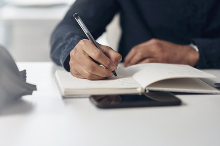 Setting deadlines for myself and my goals. an unrecognizable businessman sitting alone in his office and writing notes in a notebook.の写真素材
