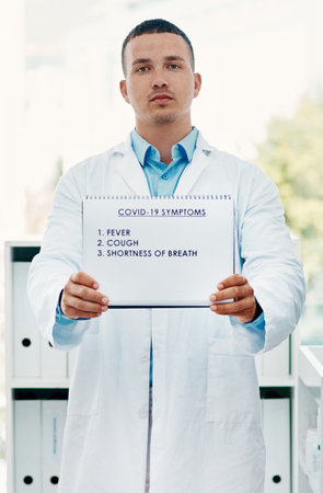 It starts with these signs. Portrait of a young scientist holding a sign with a list of COVID-19 symptoms on it in a modern laboratory.の写真素材