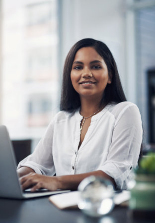 Success lies in the path of those who show dedication. Portrait of a young businesswoman working on a laptop in an office.の写真素材