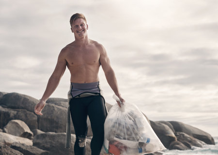 My work here is done. a man carrying a bag of trash after cleaning up the beach.の写真素材