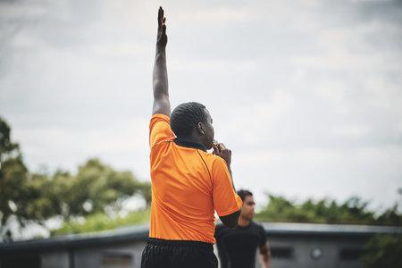 He shoots and scores. a referee blowing his whistle while lifting his hand up in the middle of a rugby match on a field during the day.の写真素材