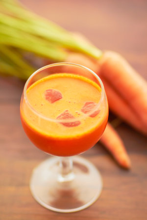 Carrot juice, vegetable and healthy food or drink with color, art and nutritionist creativity. Vegan smoothie or orange liquid in glass for wellness, diet or nutrition on a wooden table with iceの写真素材