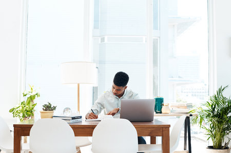 Work hard until success happens. a young businessman using a laptop and going over paperwork in a modern office.の写真素材