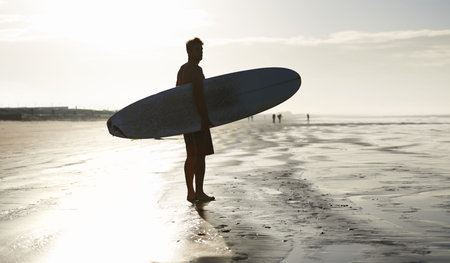 Waiting for the tide to come in. A handsome young surfer at the beach craving a good wave.の写真素材