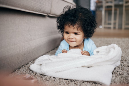 Keeping her entertained with the small things. an adorable little girl lying on the living room floor at home and playing with the laundry.の写真素材