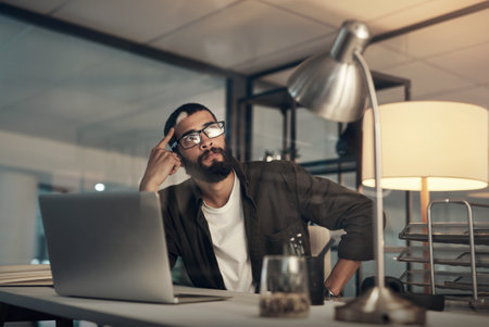 The closer to finishing the less I seem to focus. a young businessman looking uncertain while working late at night in a modern office.の写真素材