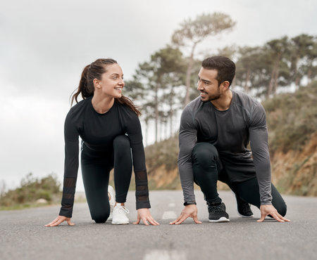 Lets race. Full length shot of two young athletes crouched down in a starters position before exercising outside.の写真素材
