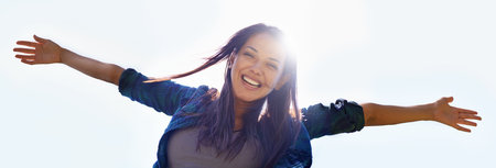 Portrait, sky and open arms with a woman outdoor in nature to celebrate a life of financial freedom in summer from below. Smile, banner and wellness with a happy young female person with lens flareの写真素材
