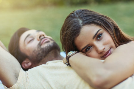 I can hear his heart beating for me. Portrait of an affectionate young couple lying outside on the lawn together.の写真素材