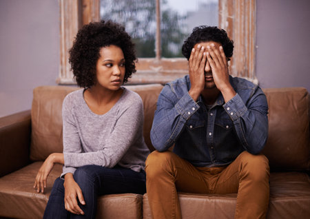 Divorce, fight and couple on a couch, depression and affair with partners at home, relationship problem and marriage. Anxiety, man and woman with conflict, frustration and cheating with mental healthの写真素材