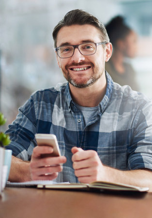 I prefer staying hands-on. Portrait of a mature businessman texting on a cellphone in an office.の写真素材