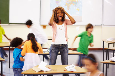 Stress, teacher screaming and black woman in classroom with children running around. Education, headache and female person shouting with burnout, tired or fatigue with kids in busy class at school.の写真素材
