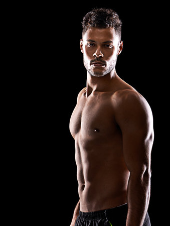 They fit in where you stand out. Studio portrait of a handsome bare-chested young athlete standing in the shadows.の写真素材