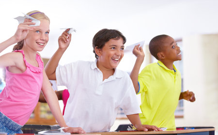 Giving their teacher grief. Three students throwing paper planes in class.