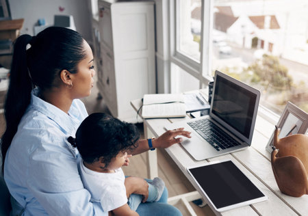 Teaching her the basics already. a young mother caring for her baby girl while working from home.の写真素材