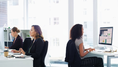 Get focused and get it done. a group of young businesswomen using their computers in a modern office.の写真素材