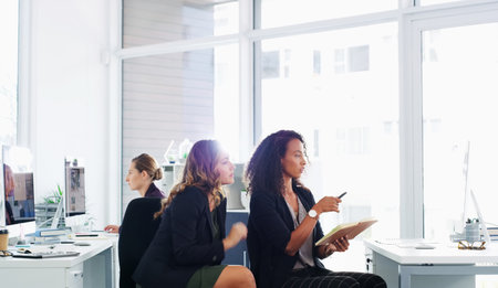 Everyone has something they can teach you. two young businesswomen using a computer together in a modern office.の写真素材