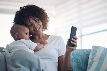 The first of many fun filled memories. a young woman taking selfies with her adorable baby girl at home.の写真素材