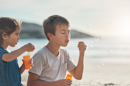 Here, let me show you. two young siblings standing together and blowing bubbles during a relaxing day on the beach.の写真素材