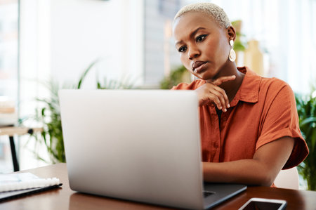 Focused hard work is the real key to success. a young businesswoman looking thoughtful while working on a laptop in an office.の写真素材